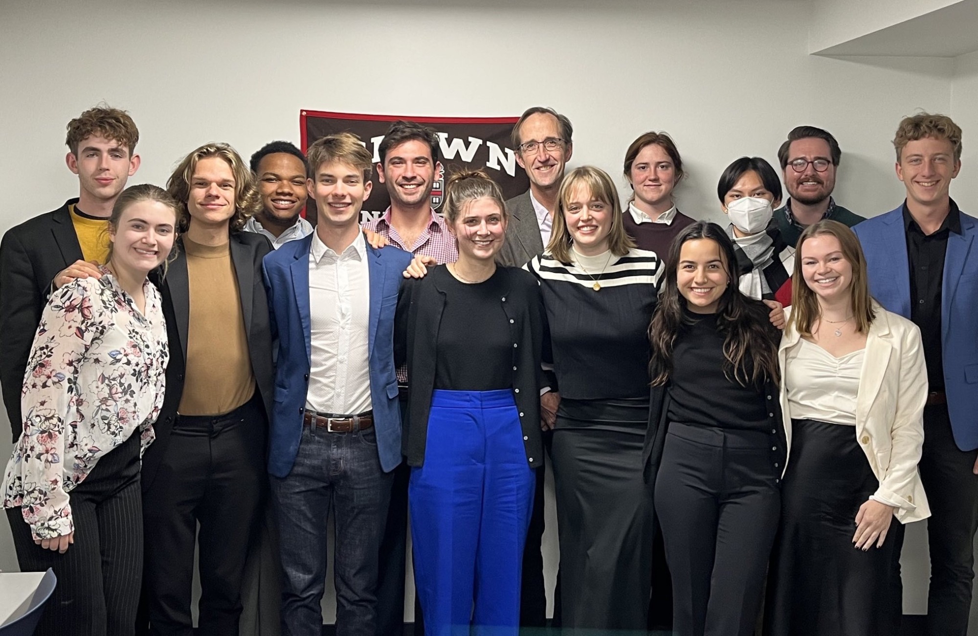 Group of undergraduate students pose in front of Brown University flag together with their professor, teaching assistant, and a postdoctoral research fellow