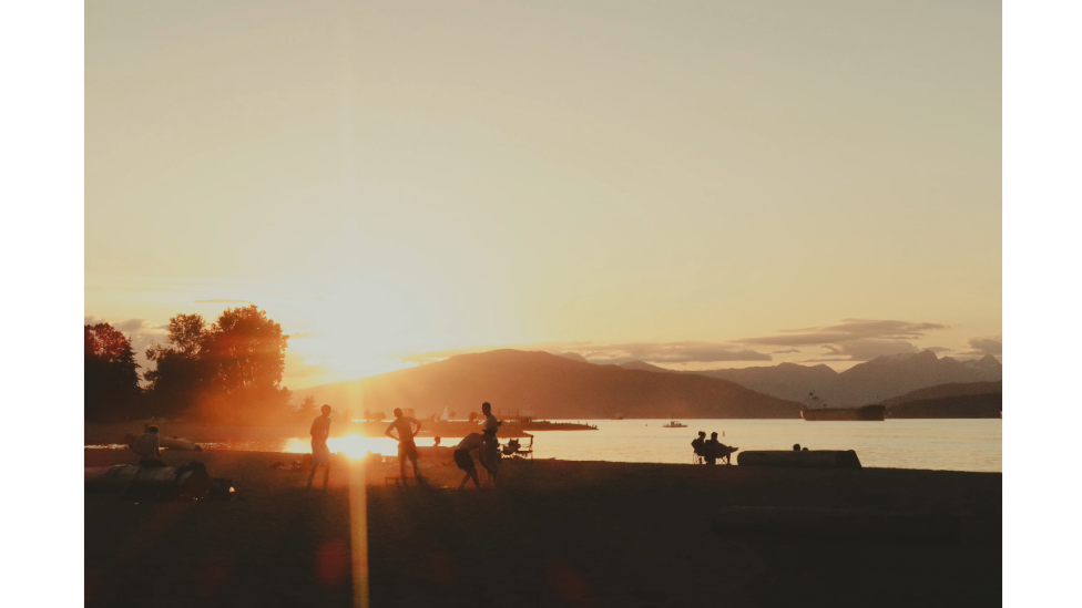 Beachgoers at sunset against the backdrop of the Burrard Inlet and Cypress Mountain