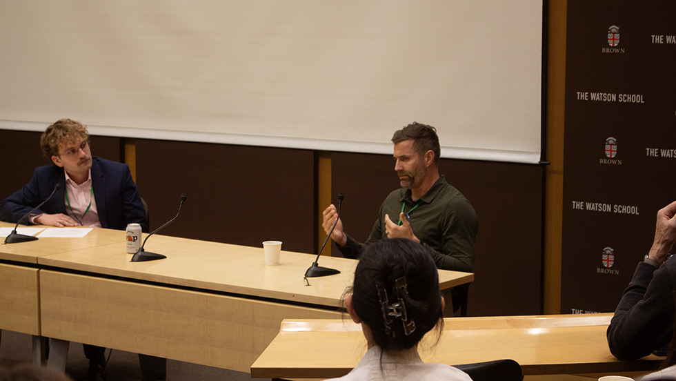 Greg Curtis speaking at table to audience in lecture hall