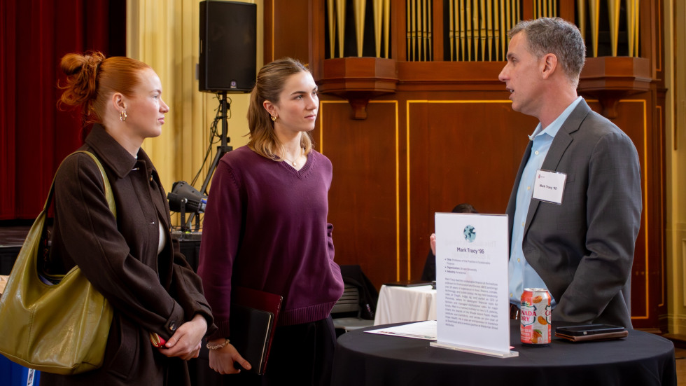 Two students speak with an alumnus