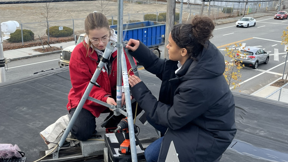 Grace Berg and Liza Marcus install an air quality monitor on a rooftop
