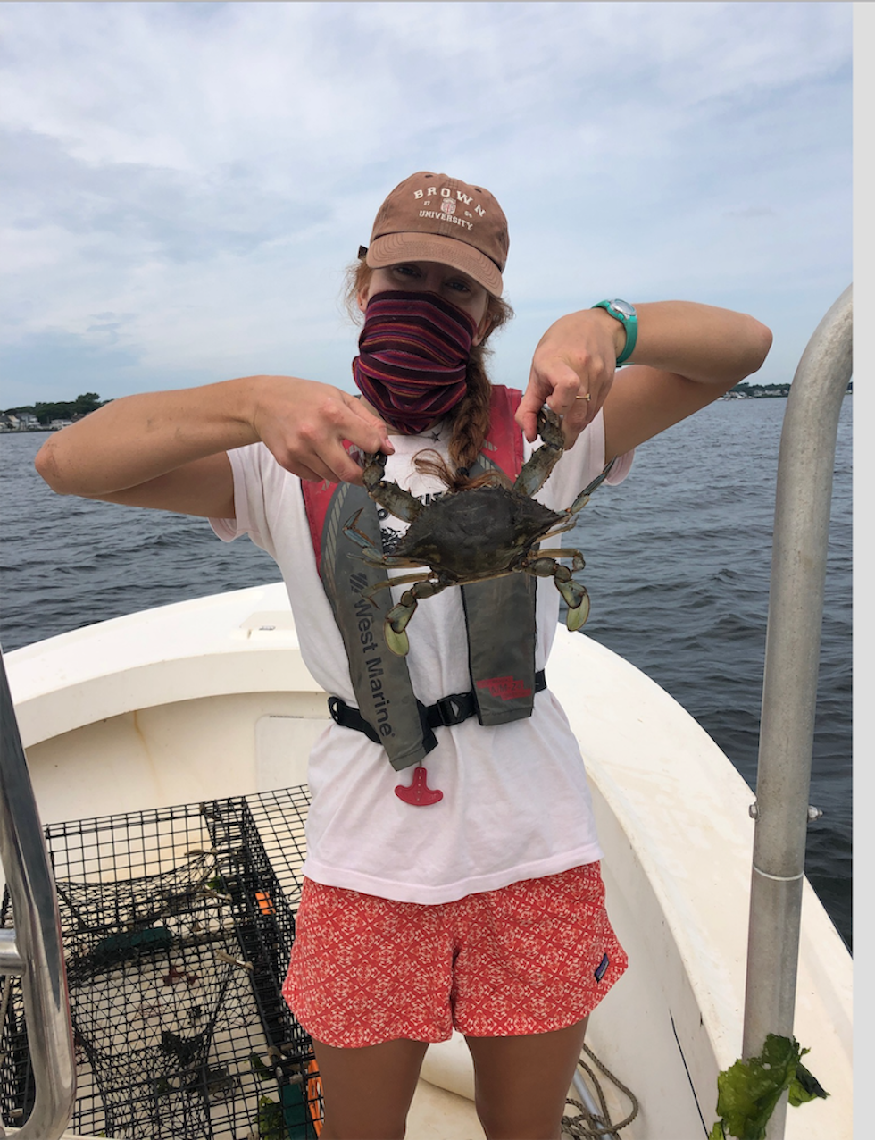 greta welch wears a face covering and holds a crab on a fishing boat